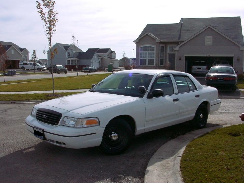 White sedan parked in driveway, house in background. Another car is in the garage