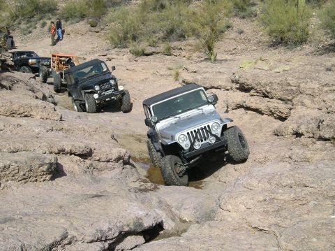 1986 Toyota Hilux - Multiple off-road vehicles navigate a challenging rocky path in a desert landscape.