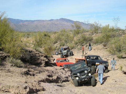 1986 Toyota Hilux - Multiple off-road vehicles traverse a challenging rocky landscape in a desert environment.