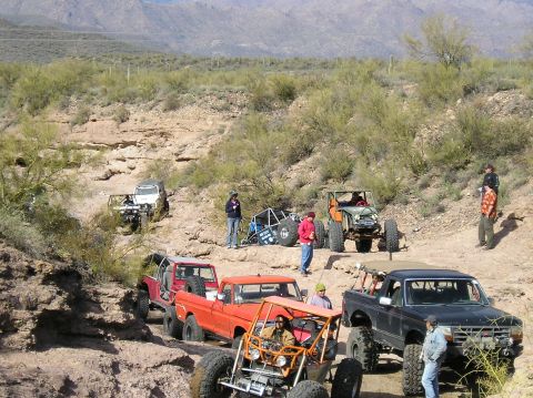 1986 Toyota Hilux - A group of off-road vehicles are seen on a challenging desert trail, with spectators gathered around.