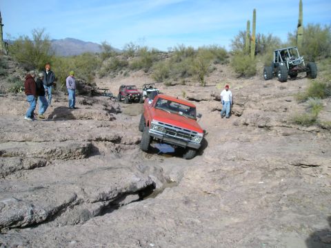 1986 Toyota Hilux - Several off-road vehicles traverse a challenging rocky course in a desert landscape.