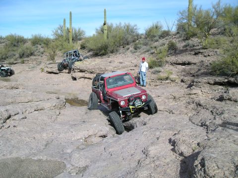 1986 Toyota Hilux - Multiple off-road vehicles traverse a rocky desert landscape under a clear blue sky.