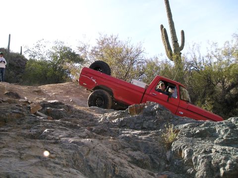 1986 Toyota Hilux - A red 1979 Ford F-150 navigates a challenging rocky terrain, with saguaro cacti in the background.