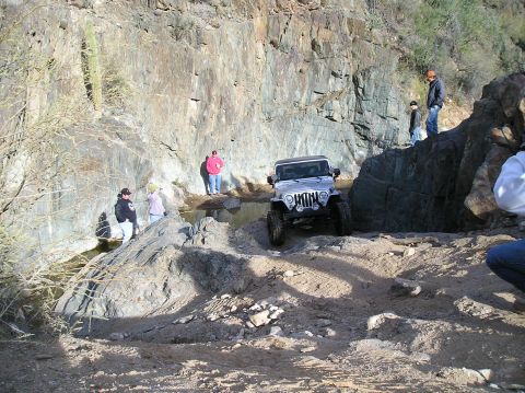 1986 Toyota Hilux - Jeep Wrangler tackling a challenging rocky trail in a desert-like environment.