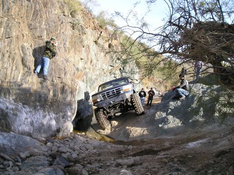 1986 Toyota Hilux - A lifted Ford truck navigates a challenging off-road course with spectators observing the action.