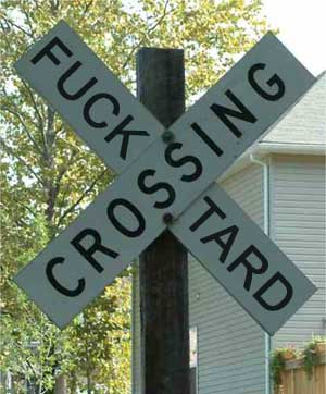 1989 Ford Bronco - A railroad crossing sign with explicit text is mounted on a wooden post, with trees and a house in the background.
