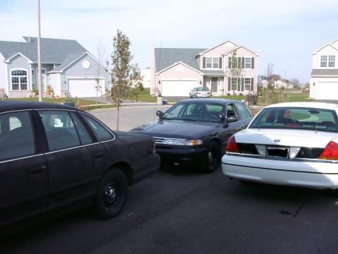 1999 Ford Crown Victoria - Three Ford Crown Victorias are parked in front of suburban houses.