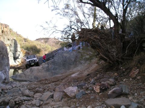 1986 Toyota Hilux - Two off-road vehicles traverse a challenging rocky landscape, with one vehicle navigating a creek bed and another partially obscured on a s…
