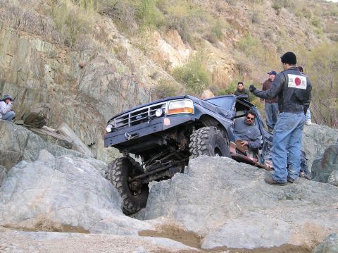 1986 Toyota Hilux - A modified Ford Bronco tackles a challenging rocky trail with several onlookers.