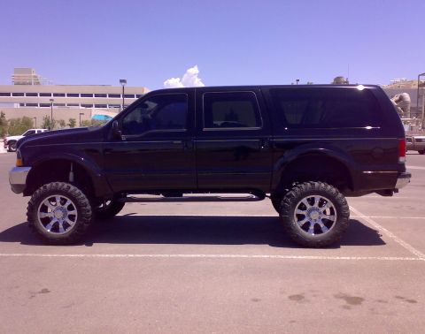 2000 Ford Excursion - A black 2000 Ford Excursion is parked in a lot, showing its lifted suspension and large chrome wheels.