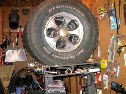 1990 Ford Bronco - A tire and wheel assembly is displayed in a cluttered garage setting with various tools and supplies visible.