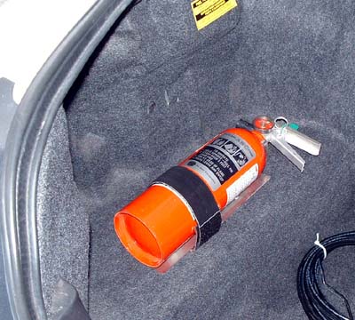 1999 Ford Crown Victoria - An orange fire extinguisher is secured with a strap inside the carpeted trunk of a vehicle.