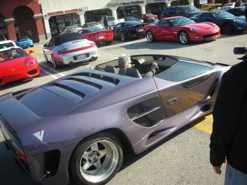 1998 Ford Crown Victoria - Several sports cars gathered in a parking lot, including a unique purple model in the foreground.
