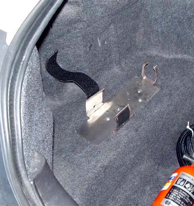 1999 Ford Crown Victoria - Trunk interior showing a metal bracket and strap for a fire extinguisher. Part of the extinguisher is visible.