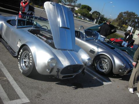 1998 Ford Crown Victoria - Two silver Shelby Cobras are parked side-by-side at an outdoor gathering.