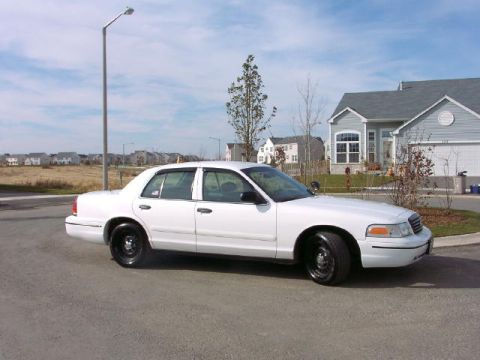 1999 Ford Crown Victoria - This white sedan is parked on a suburban street with houses in the background.