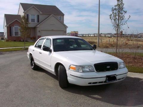 1999 Ford Crown Victoria - A white sedan is parked on an asphalt surface in front of a house.