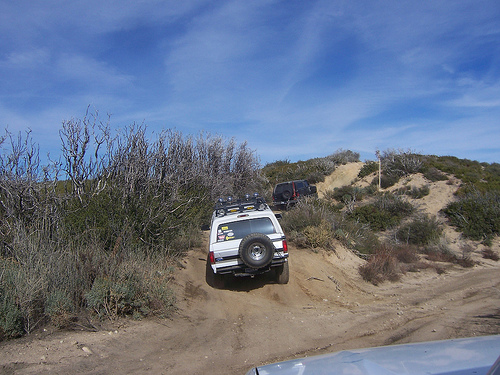 White SUV with a roof rack and spare tire on the rear, driving on a dirt trail