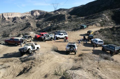 1981 Ford Bronco - A group of off-road vehicles parked on a dirt path in a mountainous desert area.