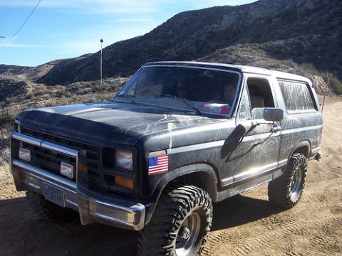 1981 Ford Bronco - A dark-colored Ford Bronco is parked on a dusty, off-road trail under a clear blue sky.