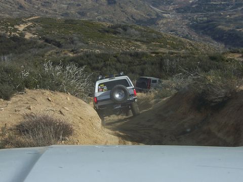 1981 Ford Bronco - A silver 1981 Ford Bronco navigates a steep dirt path off-road, with another SUV visible behind it on the trail.