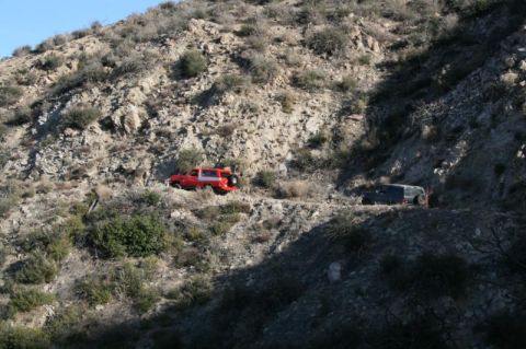 1981 Ford Bronco - Two SUVs navigate a , arid mountain trail under a clear blue sky.