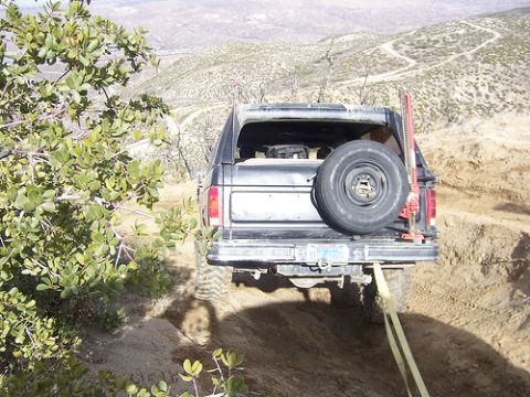 1981 Ford Bronco - Black SUV on a dirt trail with a spare tire mounted on the rear and a hi-lift jack attached.
