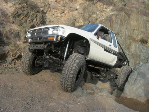 1986 Toyota Hilux - Modified Toyota pickup truck tackles a challenging rocky trail with its suspension articulated.