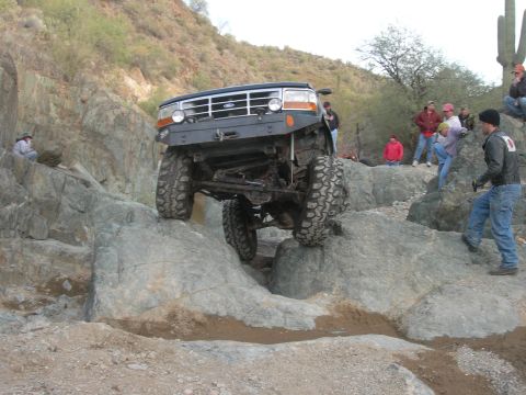 1986 Toyota Hilux - A modified 1992 Ford Bronco navigates a challenging rocky terrain with spectators watching.