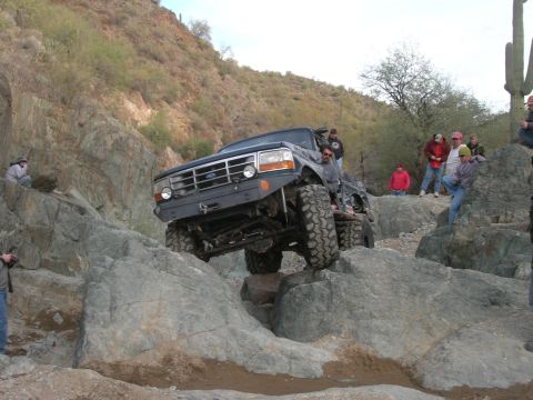 1986 Toyota Hilux - Modified Ford F-Series truck attempts a difficult rock crawl with spectators present.