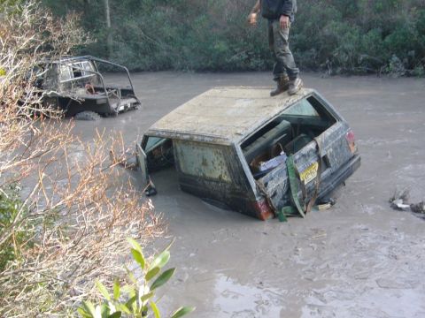 1989 Jeep Cherokee - Two off-road vehicles are submerged in thick mud, with one having a person standing on its roof.