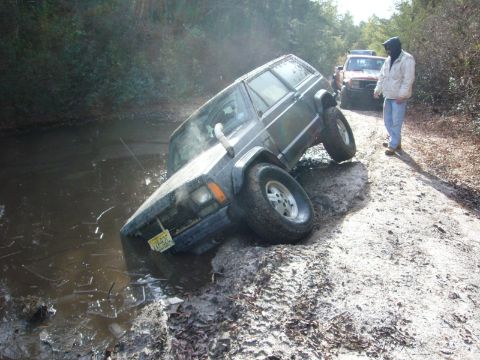 1989 Jeep Cherokee - A Jeep Cherokee is stuck in the mud, with another vehicle visible behind it on a dirt road.