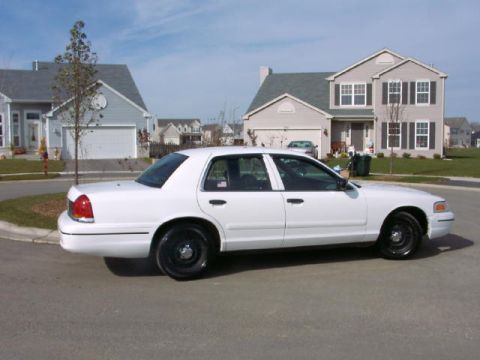 1999 Ford Crown Victoria - A white sedan is parked on a street in front of houses.