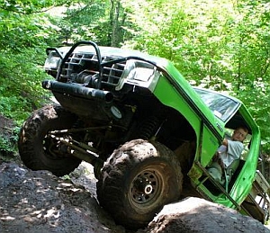 1986 Ford Bronco - This heavily modified SUV is navigating a rocky trail with its front wheels high in the air.