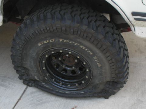 1990 Ford Bronco - A vehicle has a flat tire, showing the sidewall details of the tire.