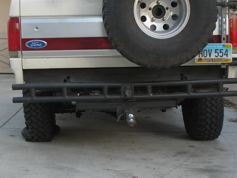Rear view of a white and silver Ford Bronco with a red stripe, spare tire mounted externally, and a custom bumper