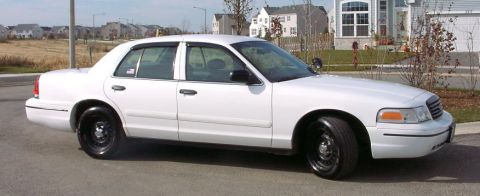 1999 Ford Crown Victoria - This white sedan is parked on a street with houses in the background.