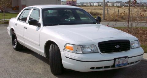 1999 Ford Crown Victoria - White sedan parked on asphalt with a clear view of its front grille and headlights.