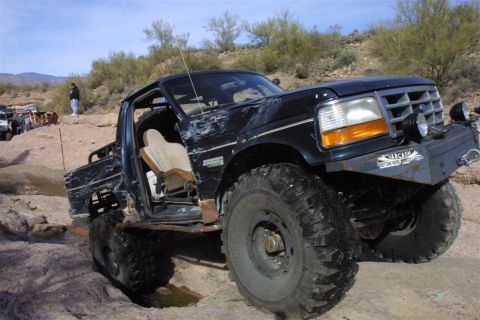 1994 Ford Bronco - This heavily modified truck appears to be from the early to mid-1990s, likely a Ford F-Series pickup, navigating a challenging off-road cou…