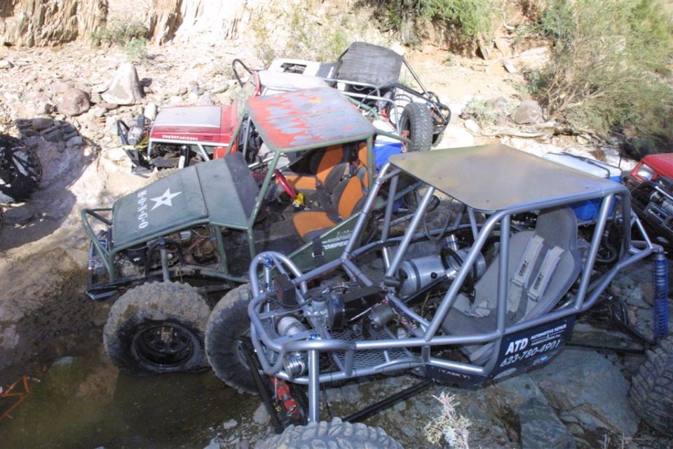 Several off-road buggies are stuck in a rocky, muddy area. One has a star and '0-D-0-0' on its side