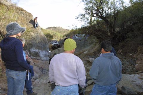 1994 Ford Bronco - Several people observe a white SUV as it climbs a challenging off-road trail.