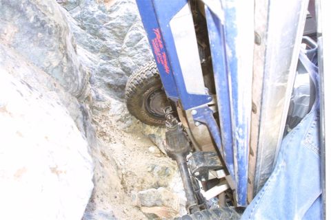 1994 Ford Bronco - A blue 1994 Ford Bronco is wedged sideways in a narrow, rocky canyon, its tire and suspension clearly visible.