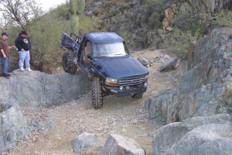 1994 Ford Bronco - A modified pickup truck tackles a challenging off-road course with two onlookers.