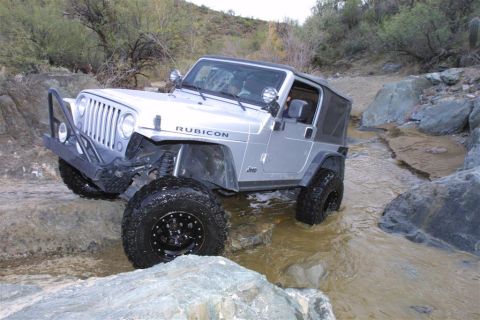 1994 Ford Bronco - Silver Jeep Wrangler Rubicon navigates a rocky stream bed during an off-road excursion.