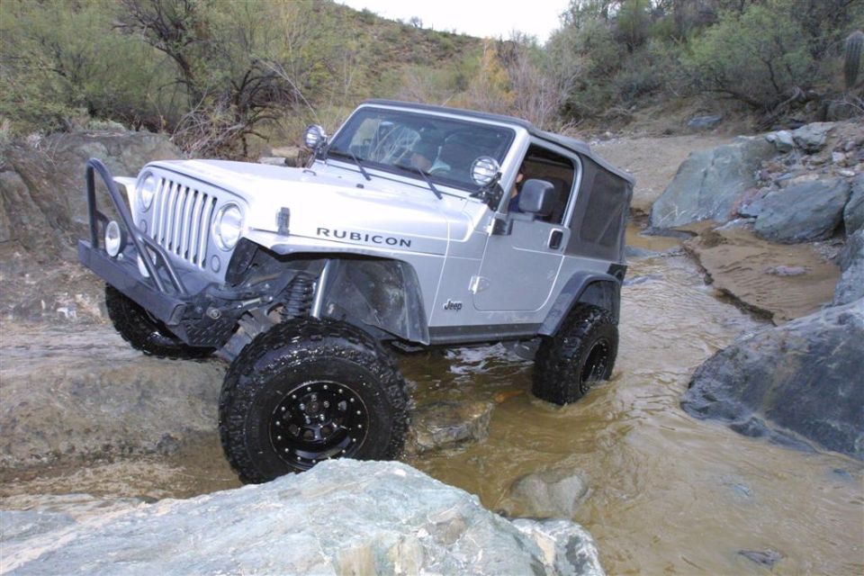 Silver Jeep Wrangler Rubicon crawling over rocks in a desert creek crossing