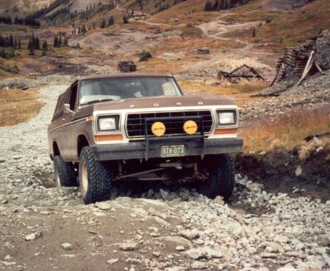 1979 Ford Bronco - Ford Bronco navigating a rough, rocky mountain path with abandoned structures in the background.