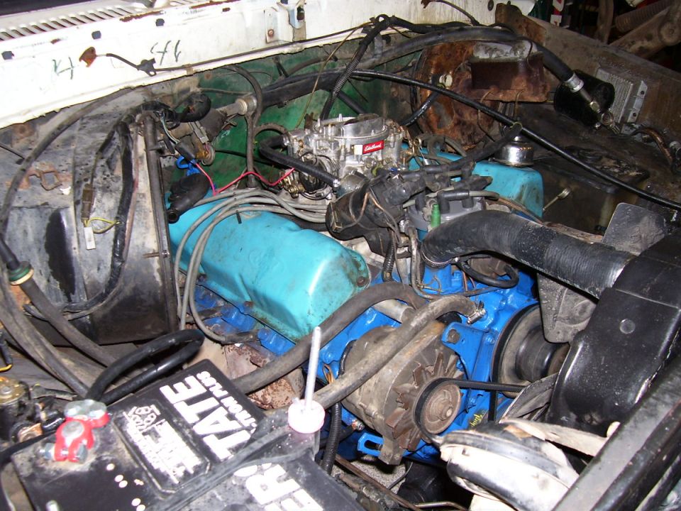 Engine bay with blue valve covers, a carburetor, and a battery
