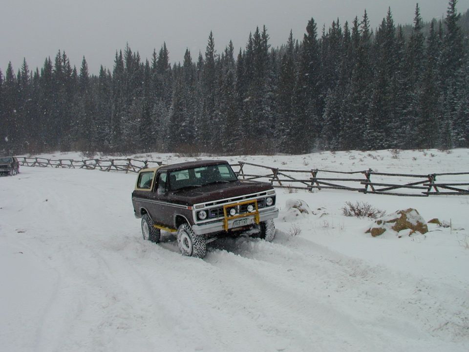 Maroon Ford Bronco with yellow brush guard driving in snow, 3/4 front view
