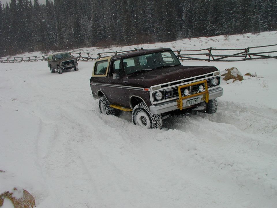 Brown Ford Bronco with yellow brush guard stuck in snow, another vehicle behind