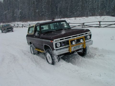 1979 Ford Bronco - A brown 1979 Ford Bronco navigates a snowy landscape, with another vehicle visible in the background.